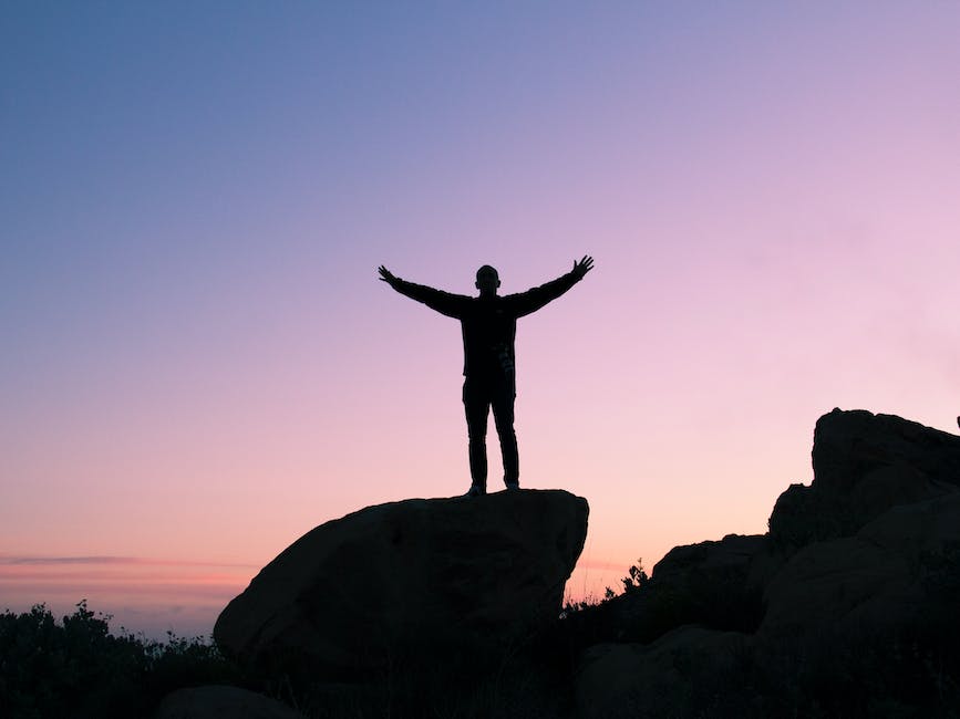 A person standing on a hill, surrounded by beautiful nature, with arms open wide, symbolizing the feeling of gratitude and self-confidence.