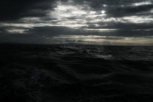 A powerful image of a person standing tall and strong, with a calm and resolute expression, against a backdrop of a stormy sea or turbulent sky. The image should symbolize the Stoic approach to navigating ingratitude, embodying resilience, inner strength, and the commitment to spreading kindness regardless of external validation.